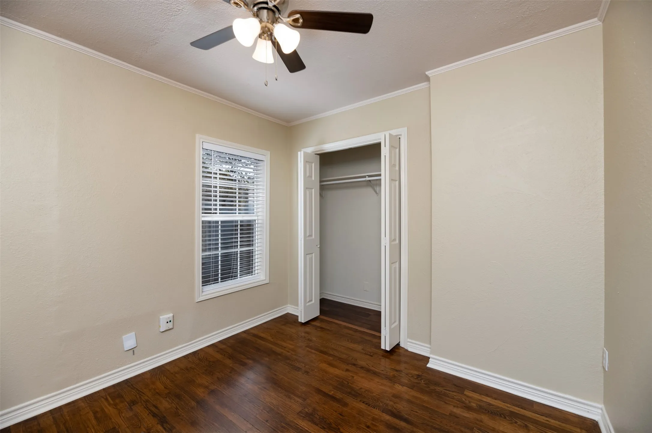 Hardwood-finish flooring, ceiling fan with integrated lighting, white trim and crown molding, and a built-in closet with bi-fold doors