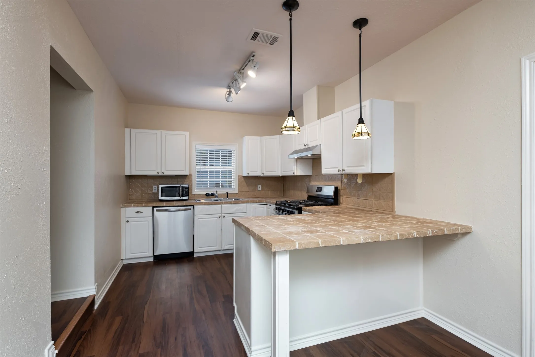 Kitchen featuring white cabinetry, wood-finish flooring, stainless steel dishwasher, a gas range, and a tile backsplash
