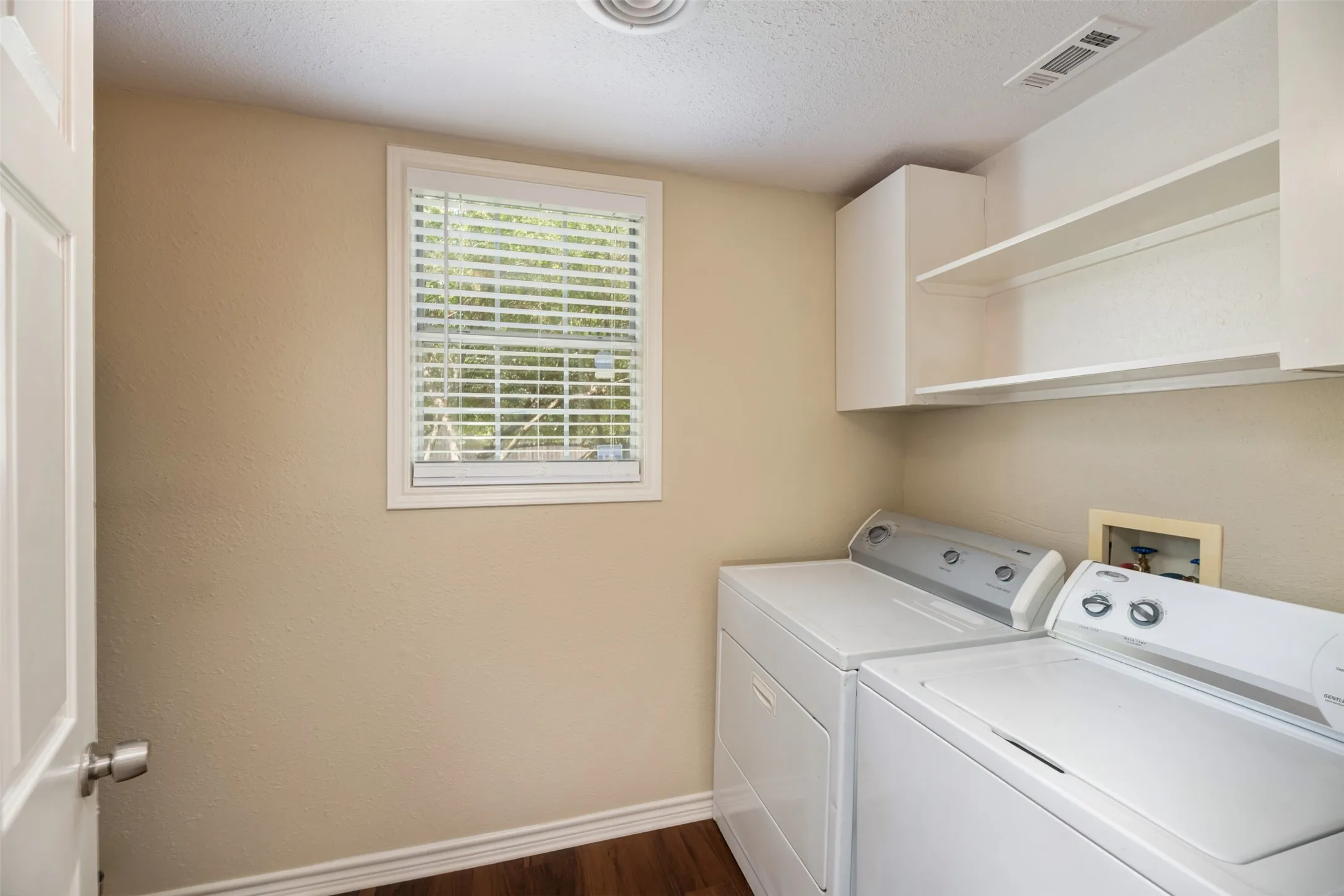 Laundry area featuring a window with blinds, white upper cabinetry, and wood-finish flooring