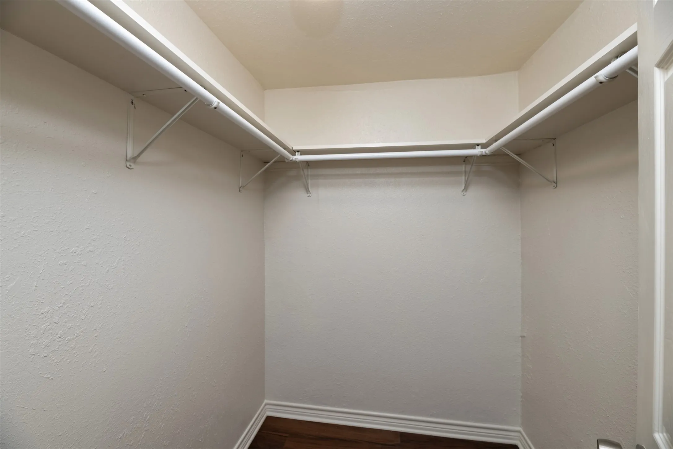Walk-in closet with white shelving, hanging rods, and wood-finish flooring