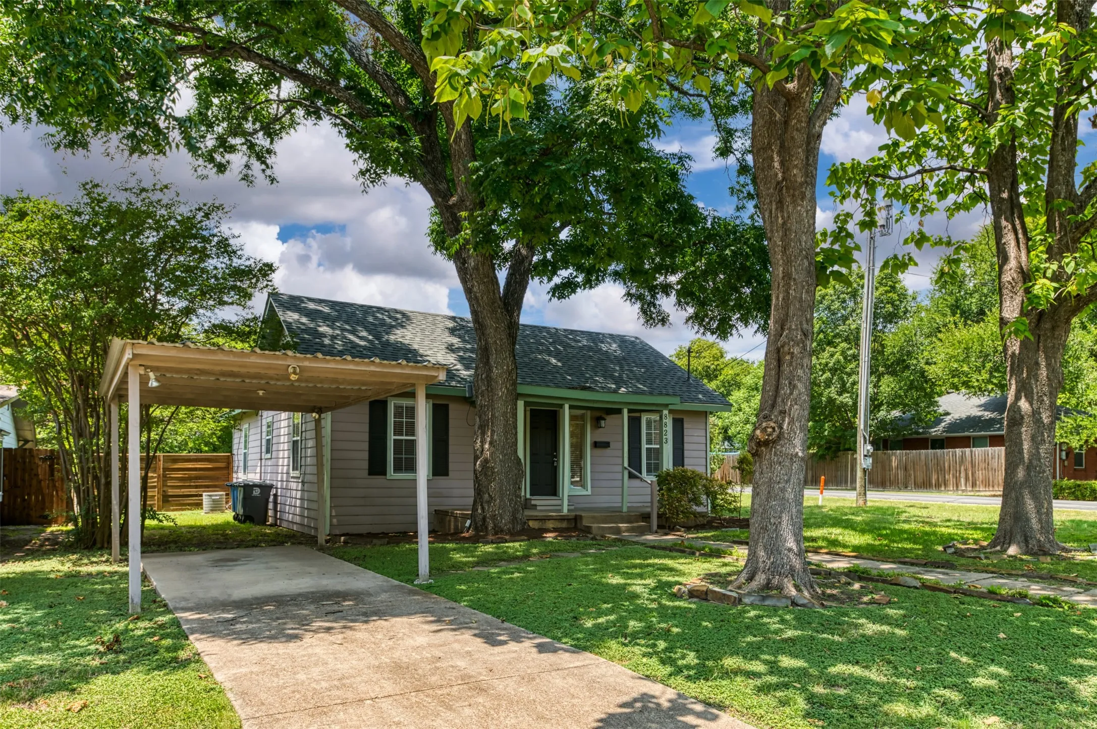 Single-story residence featuring a covered carport, a concrete driveway, and mature trees