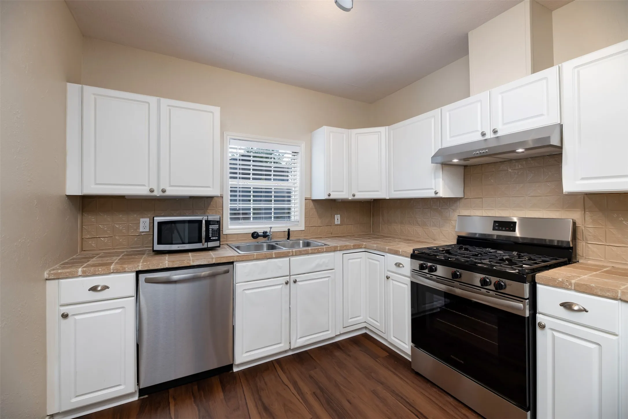 Full kitchen featuring white cabinetry, tile countertops, tile backsplash, stainless steel appliances, and wood-finish flooring