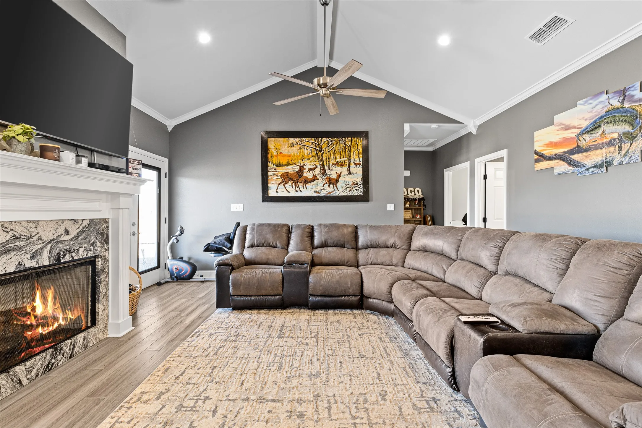Living room with vaulted ceiling, light hardwood / wood-style flooring, ornamental molding, ceiling fan, and a high end fireplace