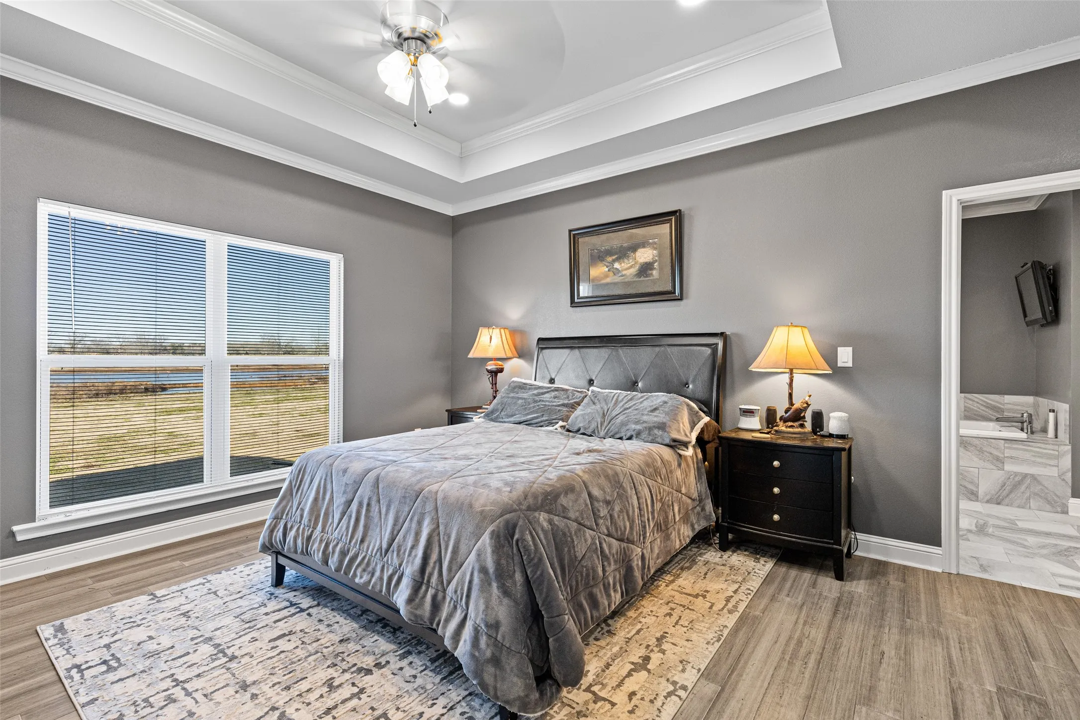 Bedroom with a raised ceiling, hardwood / wood-style flooring, connected bathroom, and ceiling fan