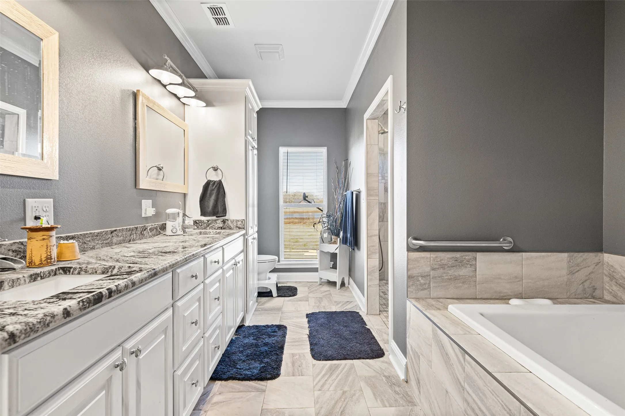 Bathroom with a relaxing tiled tub, ornamental molding, toilet, and vanity