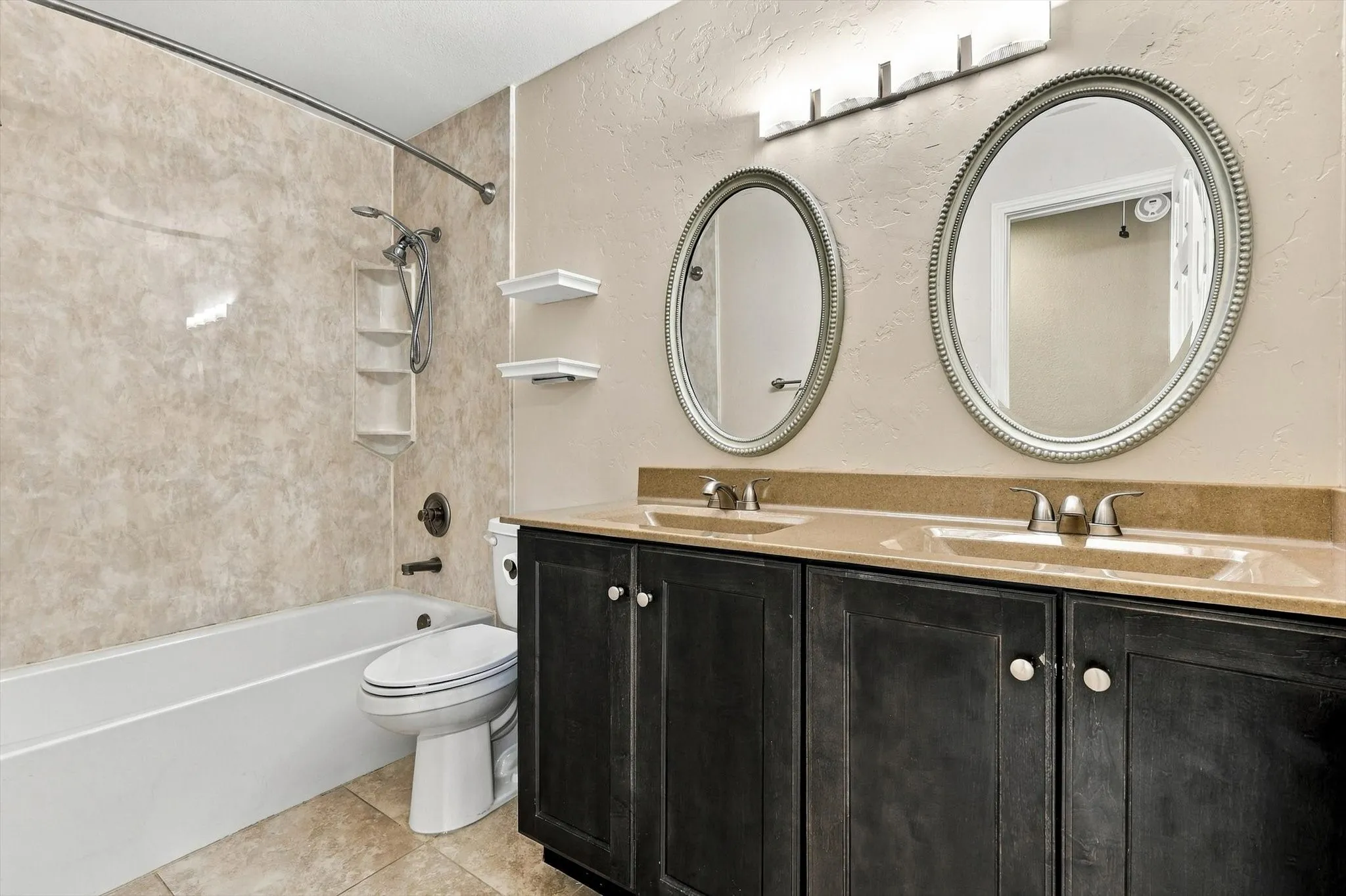Dual oval mirrors with beaded frames, a double vanity with ample storage, two undermount sinks, and a bathtub with a tiled surround