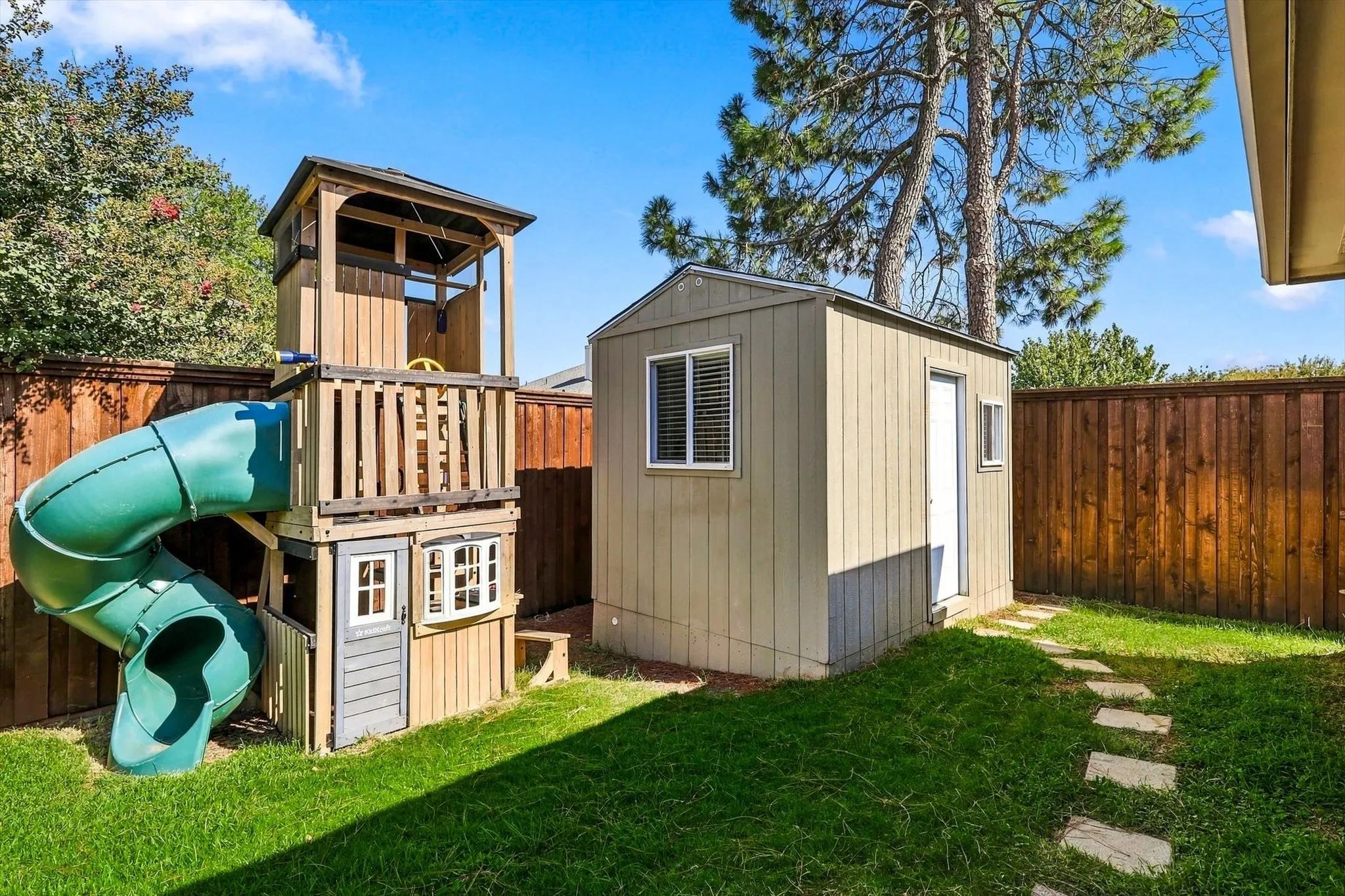 Manicured lawn with a privacy fence, stone pathway, and a detached storage shed
