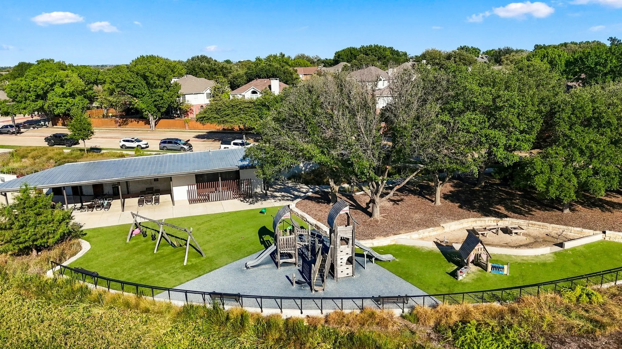 Community amenity space featuring a covered pavilion, playground with swings and slides, and a sand area