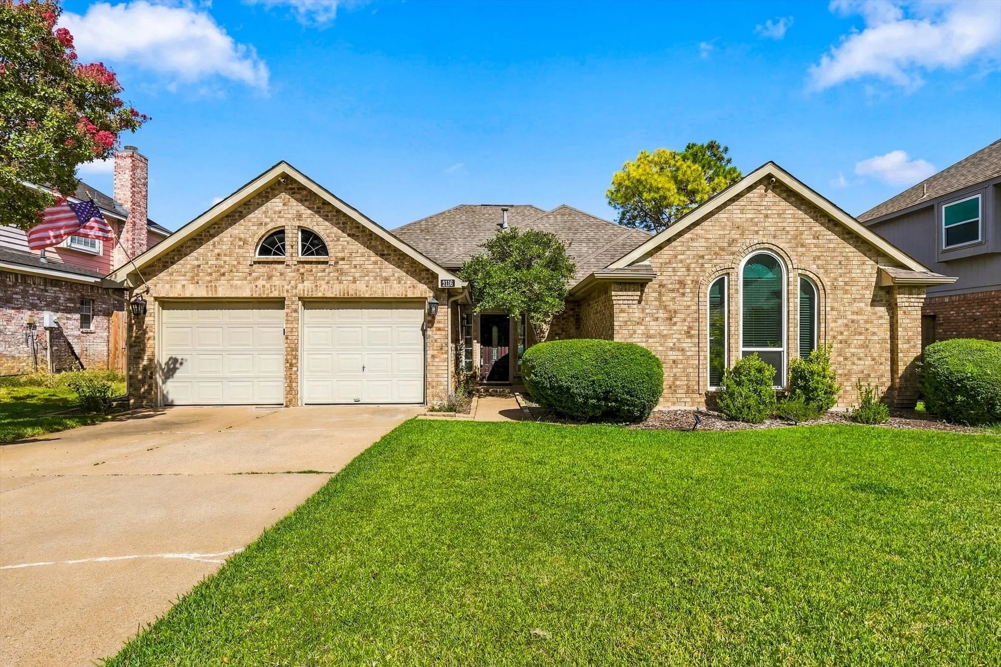 Brick exterior, gabled roofline, arched window, two-car garage, and manicured lawn