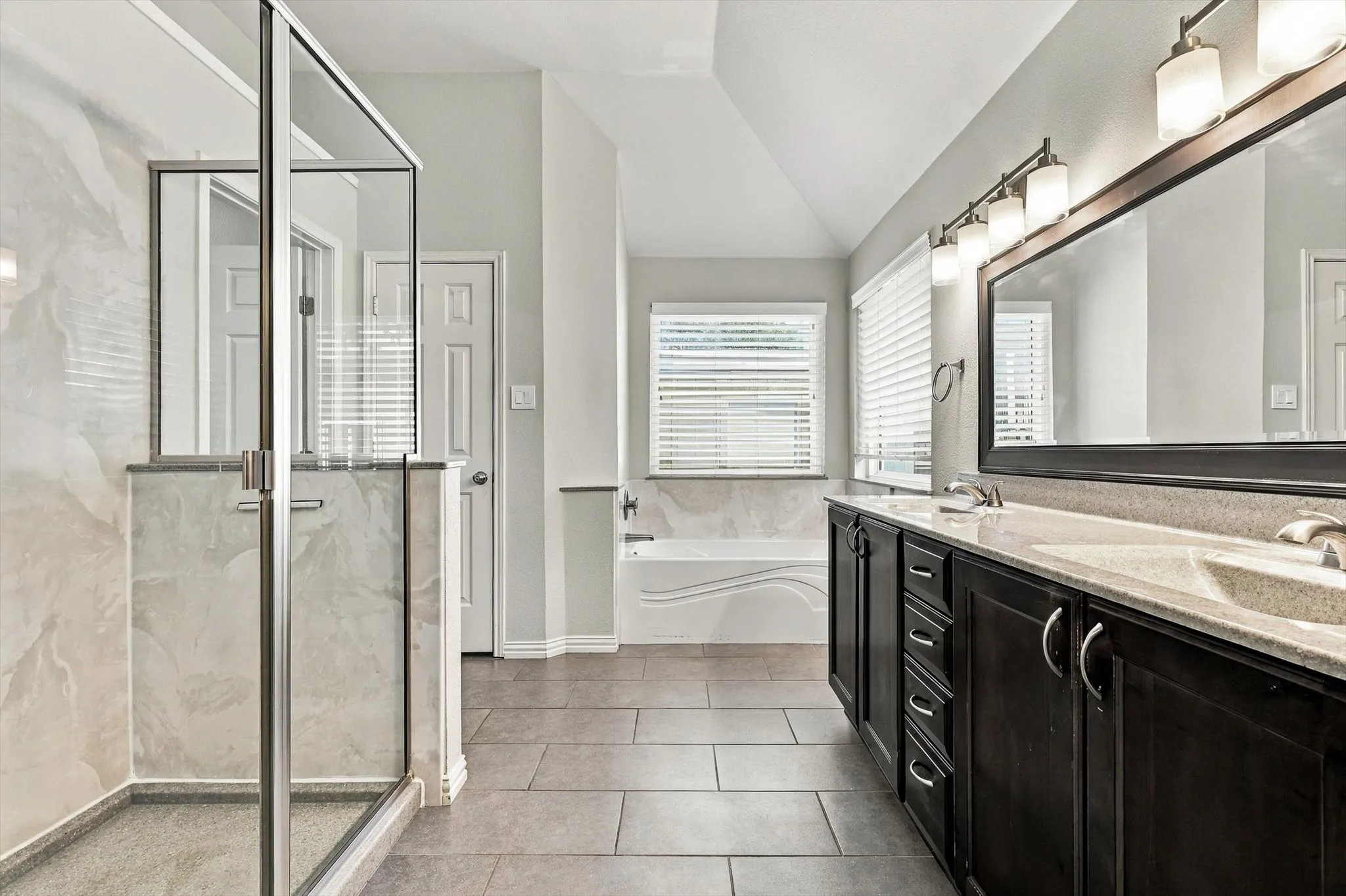 Spacious bathroom featuring a glass-enclosed shower, a separate soaking tub, and a dual-sink vanity with dark wood-finish cabinetry