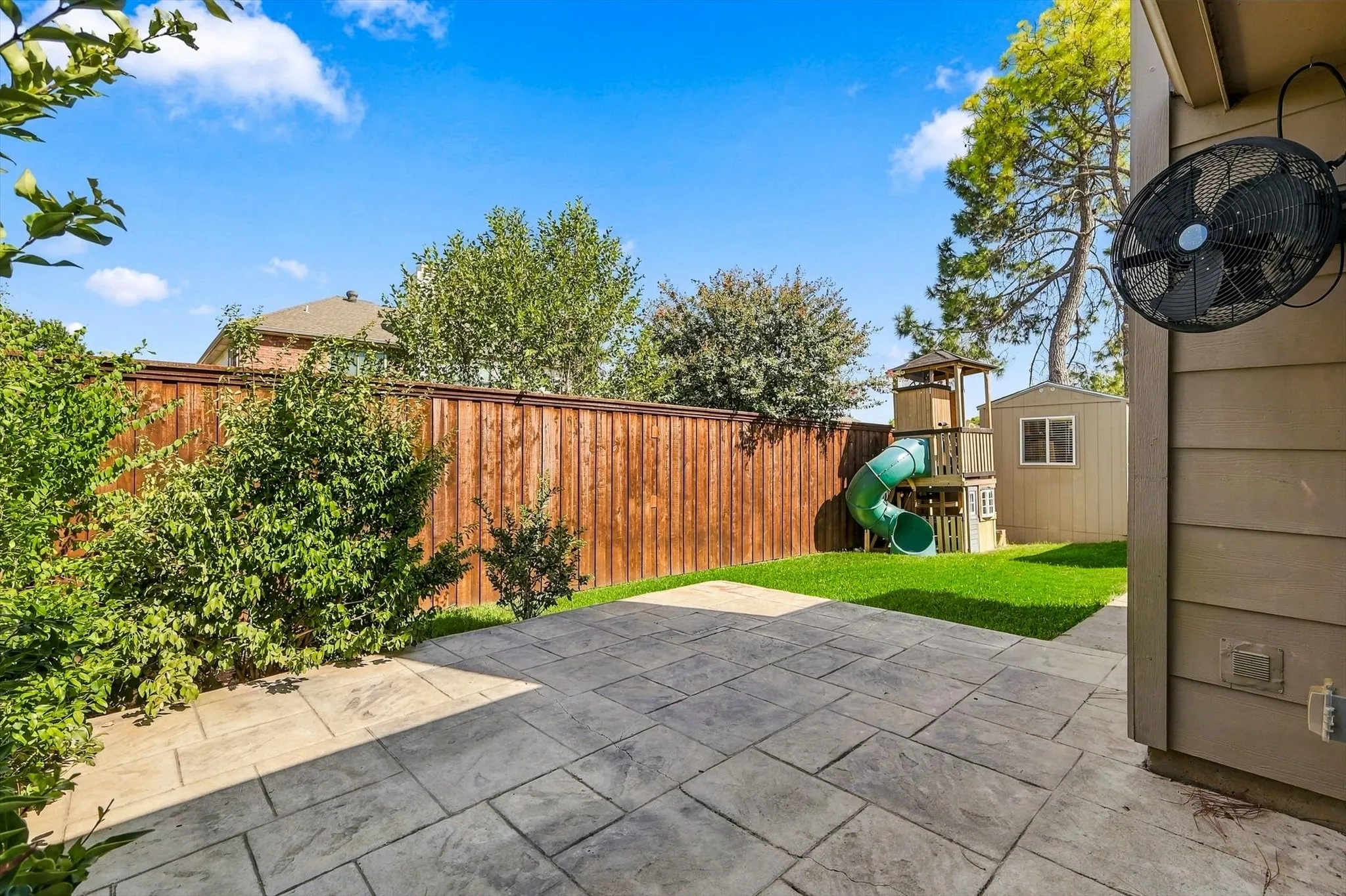 Expansive patio featuring textured pavers, manicured lawn, and privacy fencing