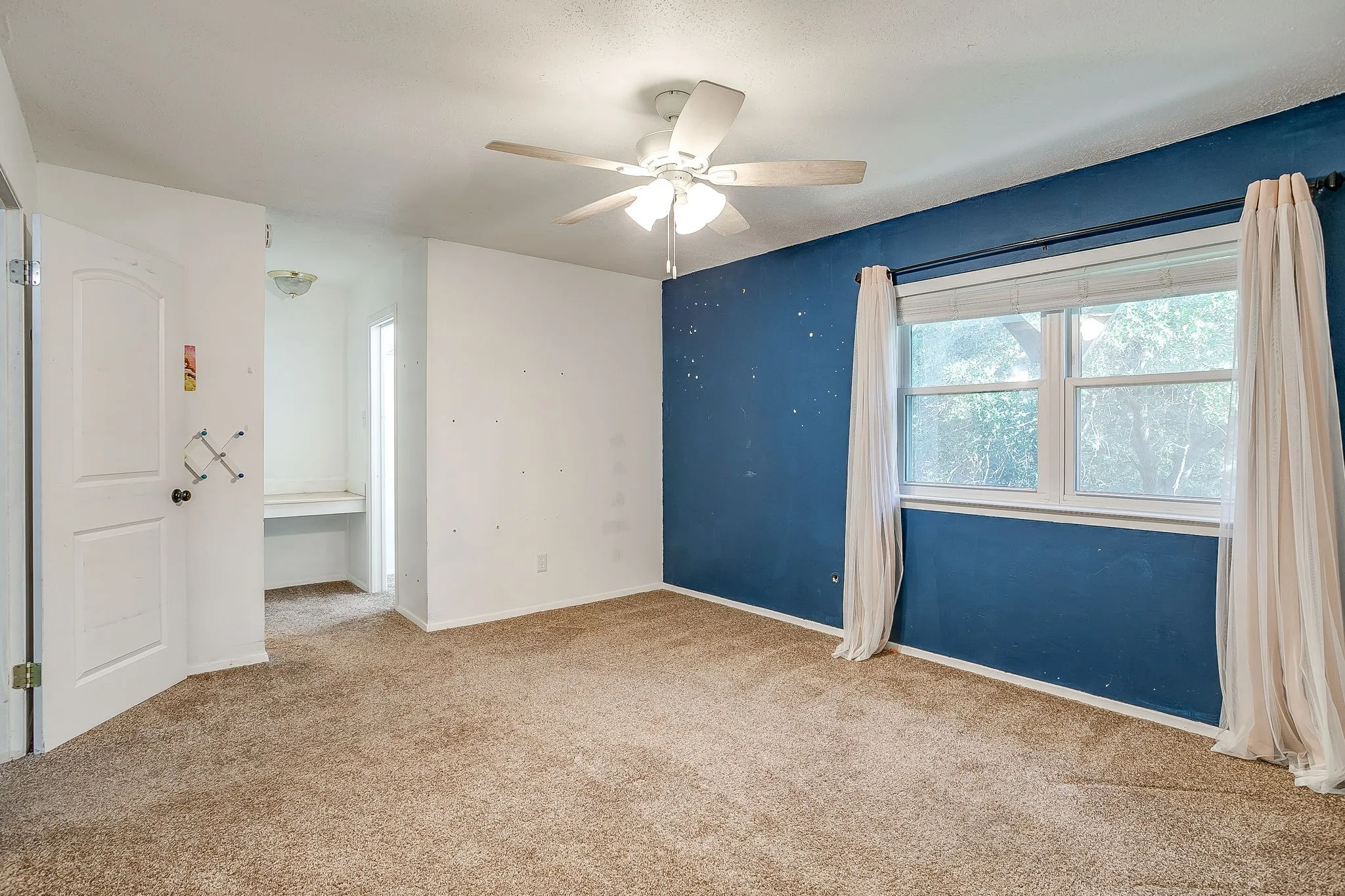 Ceiling fan with light fixture, window with drapes, carpet flooring, built-in desk, and ceiling-mounted light fixture