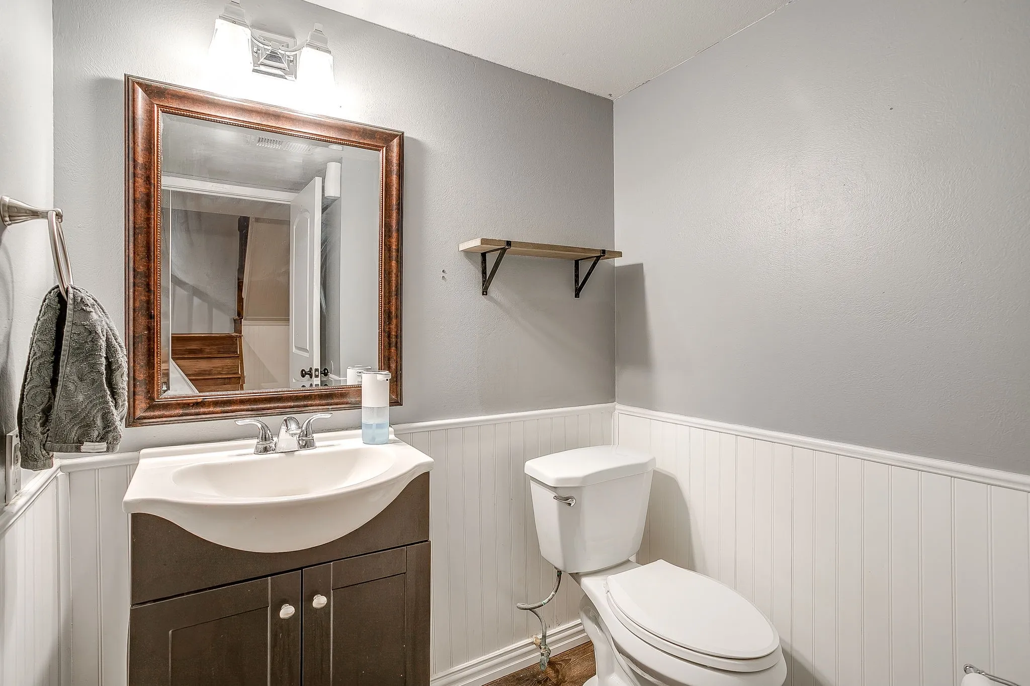 Bathroom featuring a vanity with integrated sink, wood-finish cabinet, white wainscoting, and a wall-mounted mirror