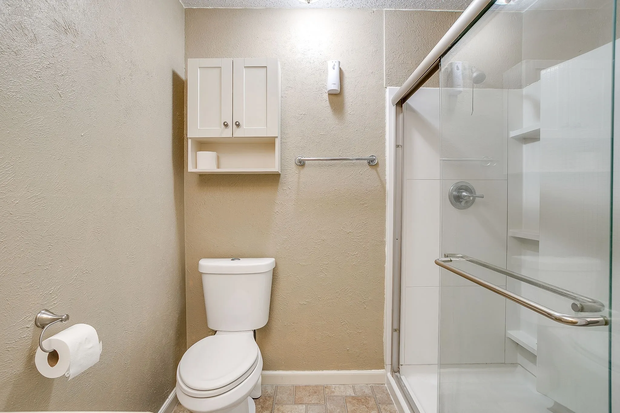Glass-enclosed shower with built-in shelving, a white toilet, and wall-mounted storage cabinetry