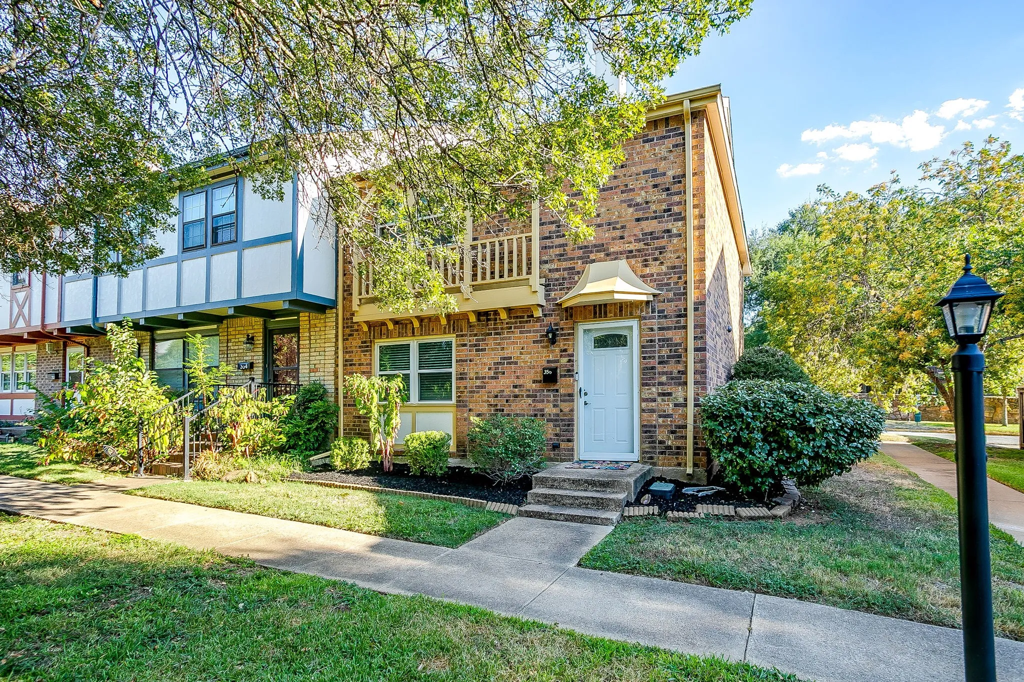 Brick facade with white front door, decorative balcony, and mature landscaping