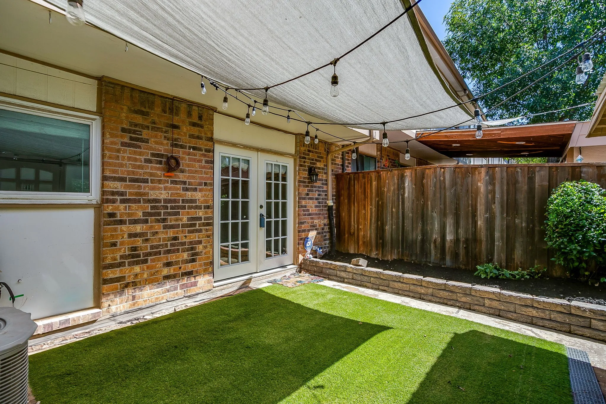Private backyard featuring a shade sail, artificial turf, brick retaining wall, and wood privacy fence