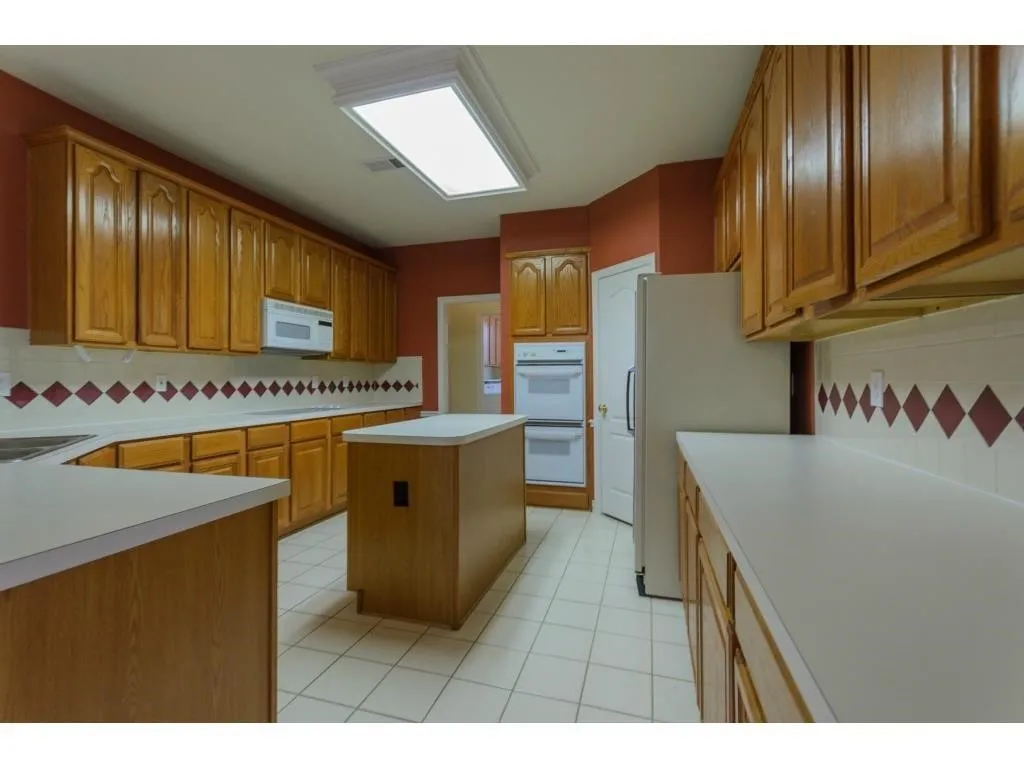 Kitchen featuring a center island, extensive light wood cabinetry, white countertops, a tiled backsplash with diamond accents, and white tile flooring