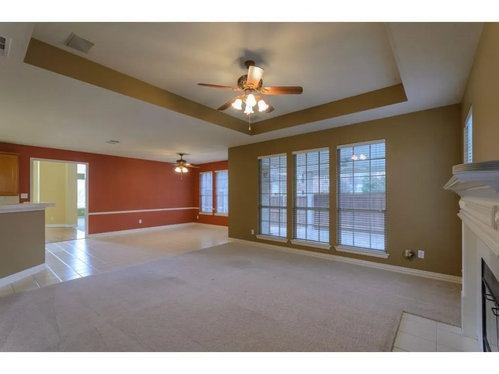 Carpeted living area with tray ceiling, ceiling fan, and multiple windows