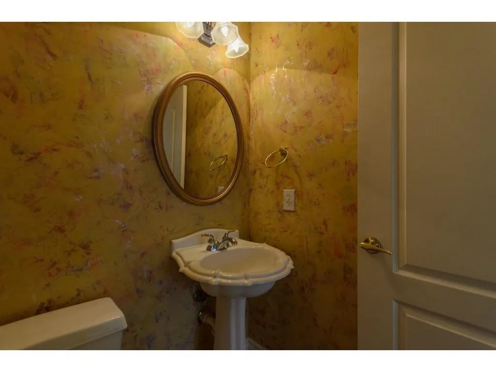 Pedestal sink with chrome-finish faucet, framed oval mirror, and wall-mounted vanity lighting