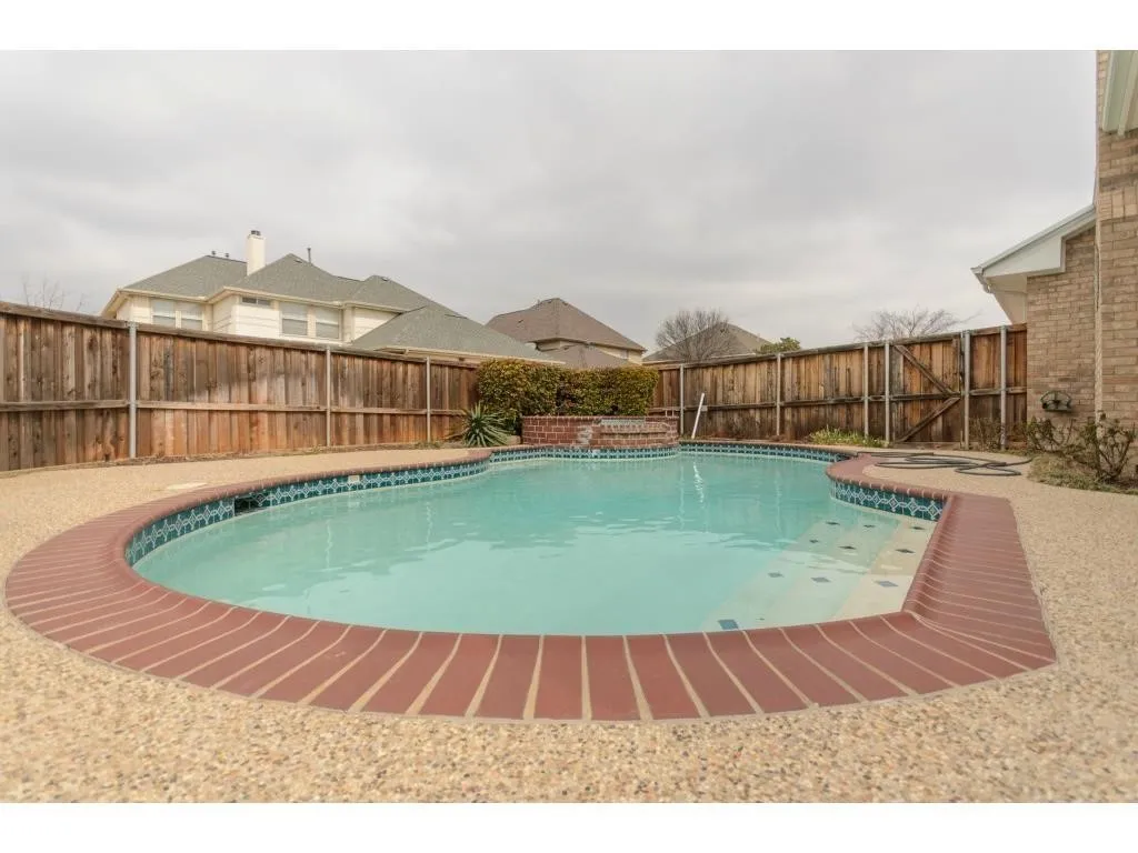 Curved swimming pool with brick coping and exposed aggregate decking