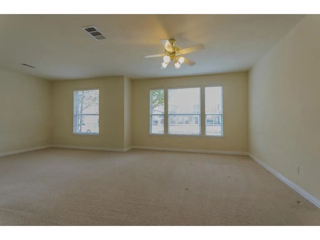 Expansive carpeted room featuring multiple windows with blinds and a ceiling fan with integrated lighting
