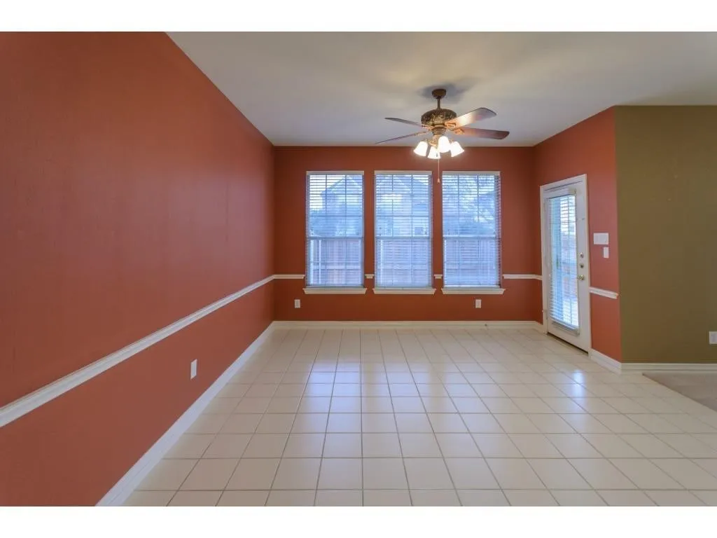 Tile flooring, decorative wall trim, multiple windows with blinds, ceiling fan with integrated lighting, and a glass-paneled door