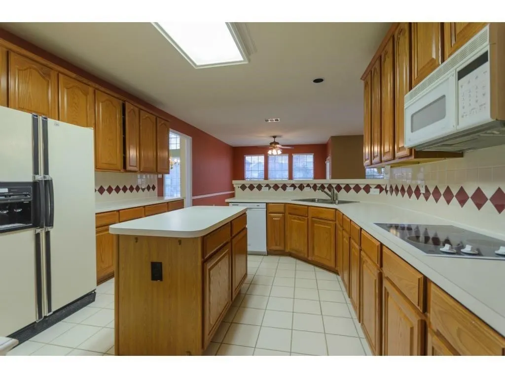 Kitchen featuring wood cabinetry, an island, white tile flooring, a built-in cooktop, and a double-basin sink