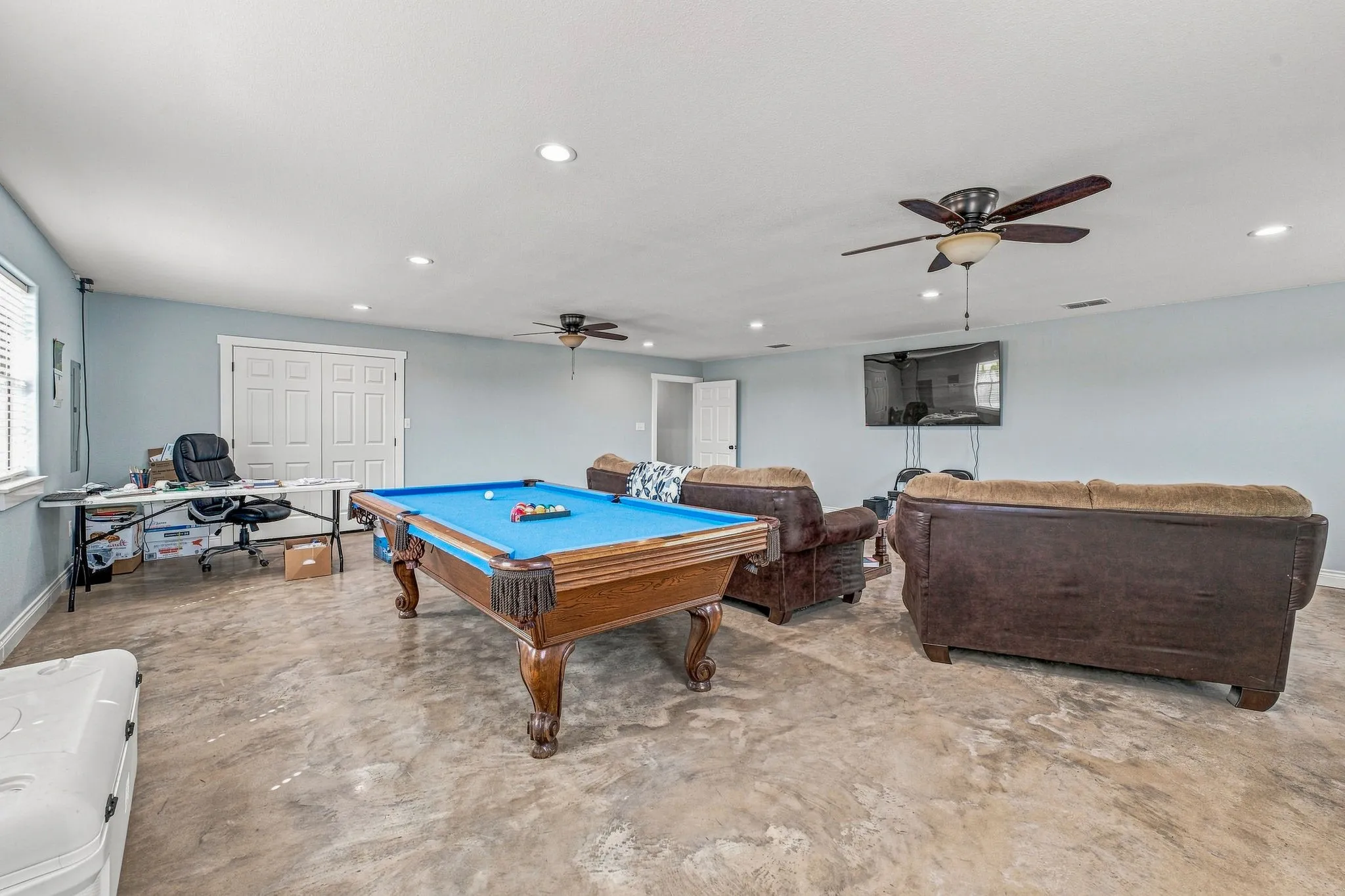 Spacious room featuring light blue walls, recessed lighting, two ceiling fans, and durable concrete flooring