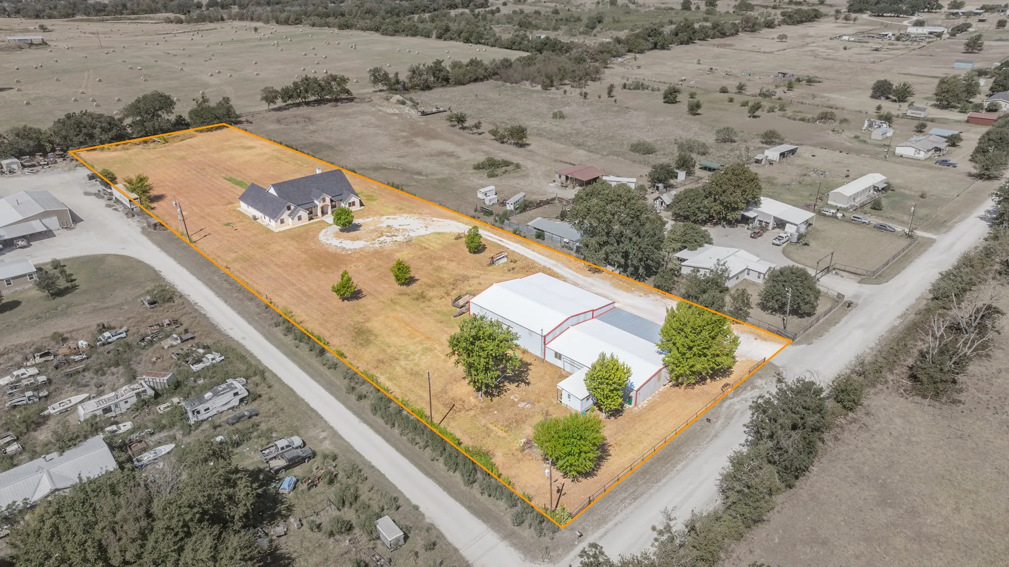 Expansive property featuring a stone exterior residence, a circular driveway, multiple outbuildings, and a large open field