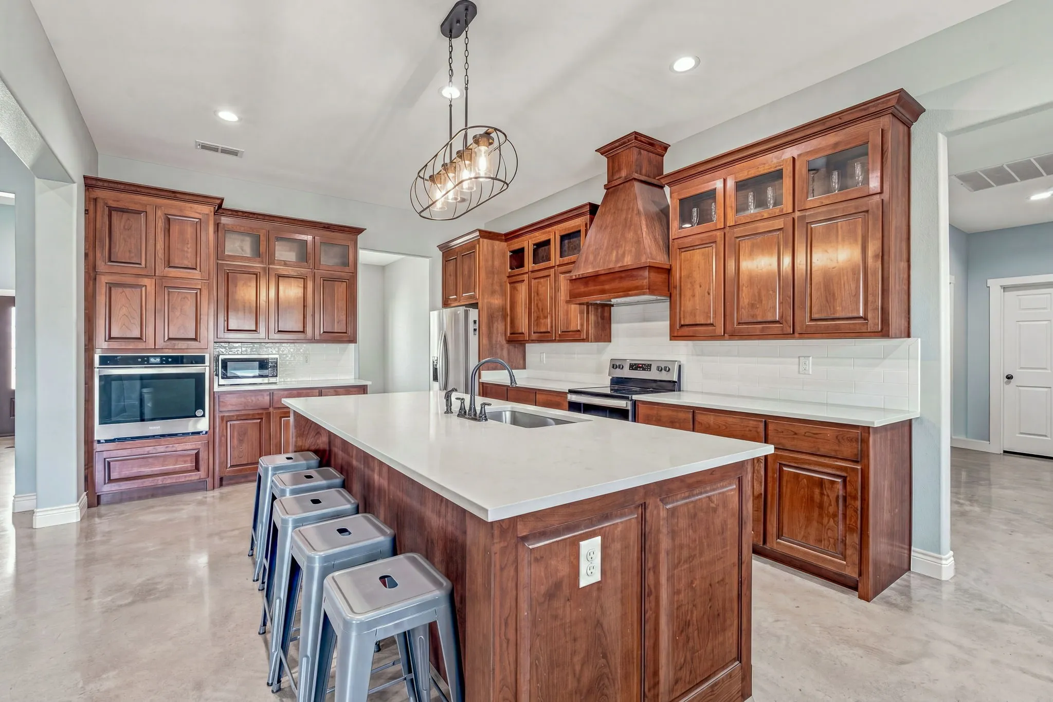 Spacious kitchen with wood cabinetry, a large center island with a light-toned countertop, a built-in oven, and a wood-finish range hood