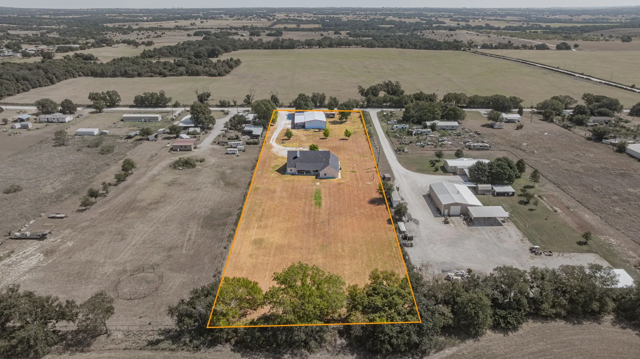 Expansive property with a detached auxiliary building, mature trees, and a long gravel driveway