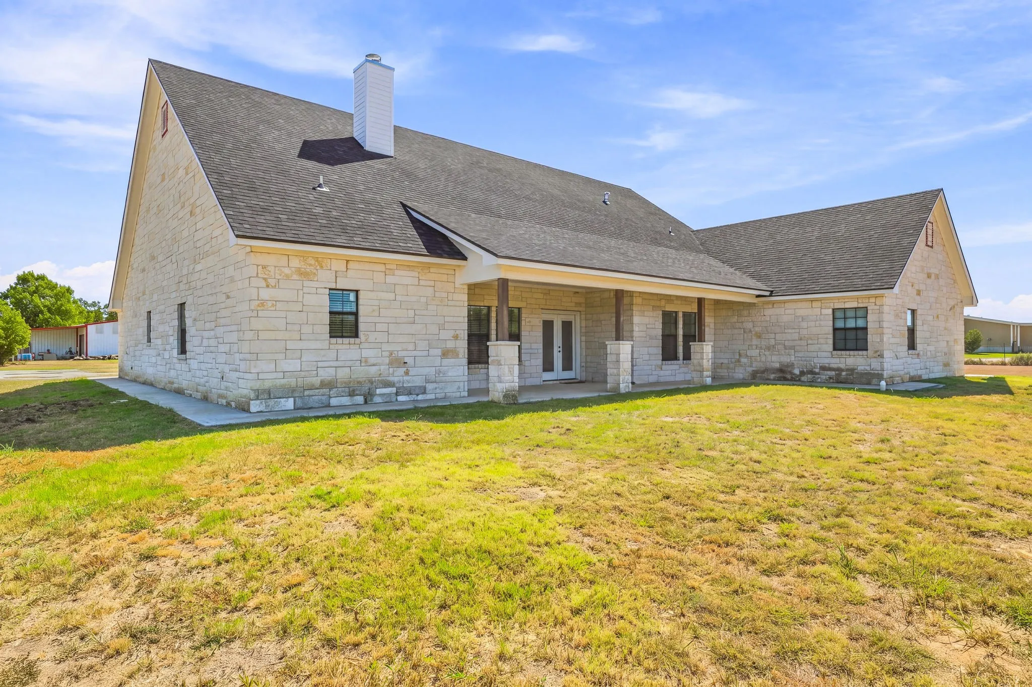 Stone exterior with a dark shingle roof, featuring a covered porch with stone pillars