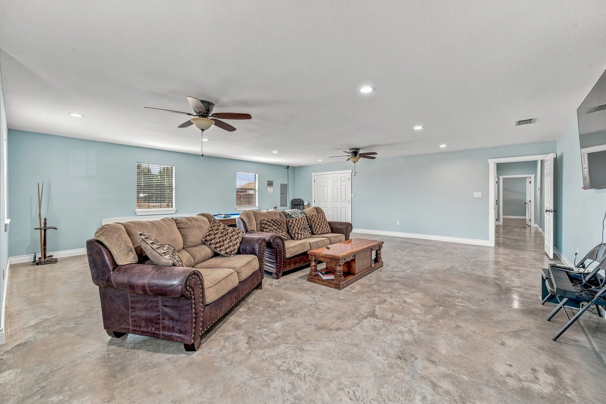 Expansive room featuring light blue walls, recessed lighting, two ceiling fans, and concrete flooring
