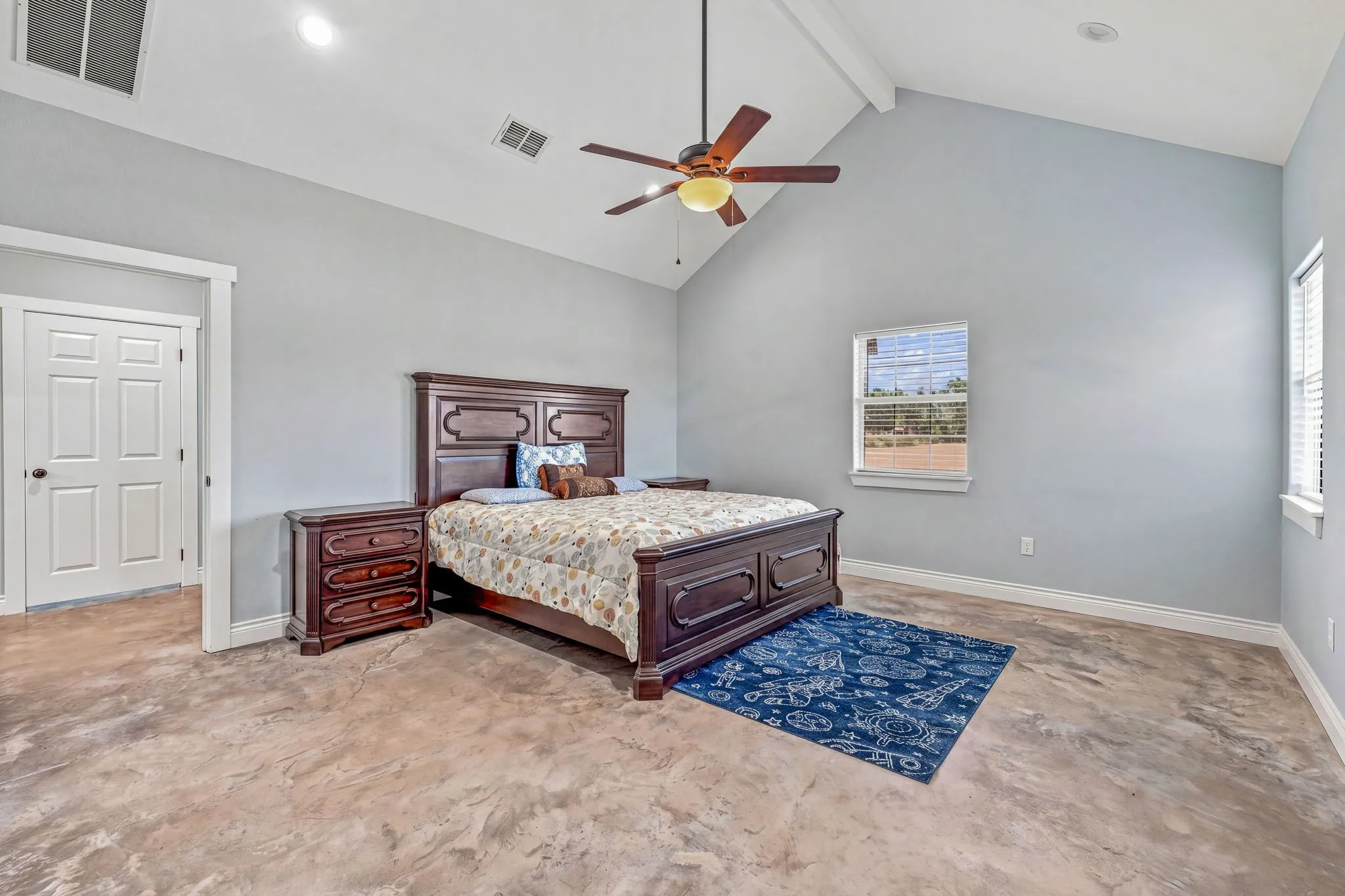 Vaulted ceiling with a ceiling fan, light gray wall paint, windows with blinds, and stained concrete flooring
