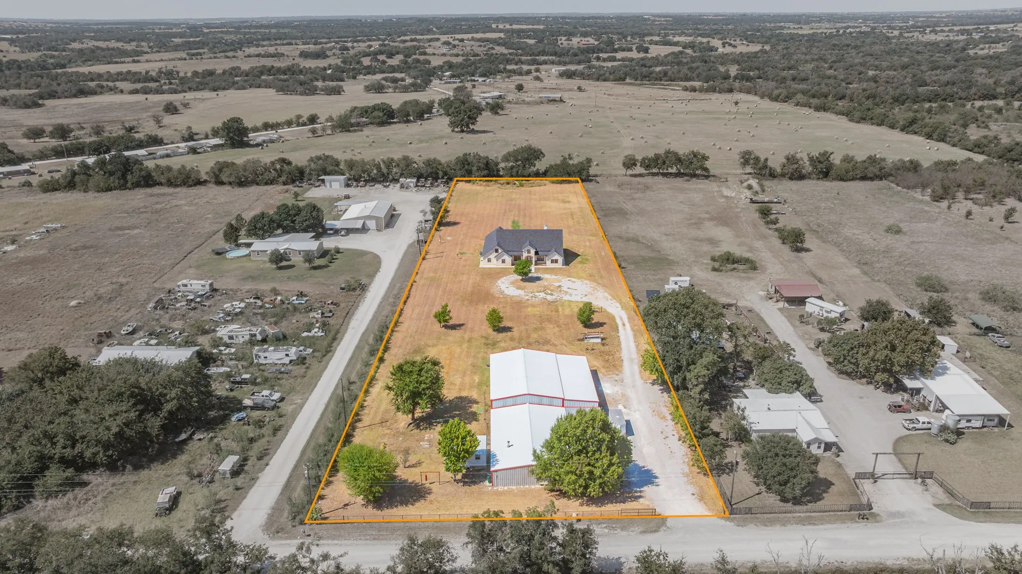 Sprawling rural property featuring a main residence, a large outbuilding, and expansive natural terrain