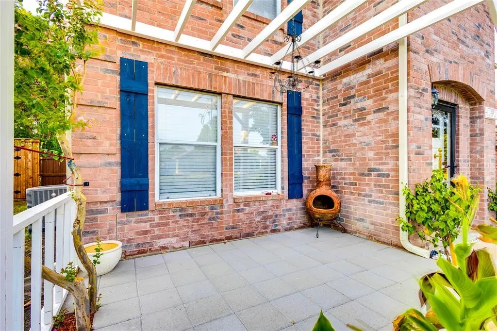 Brick exterior with blue shutters, covered patio, white pergola, and arched entryway