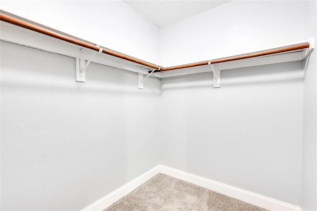 Corner closet featuring wood-finish hanging rods and white shelving
