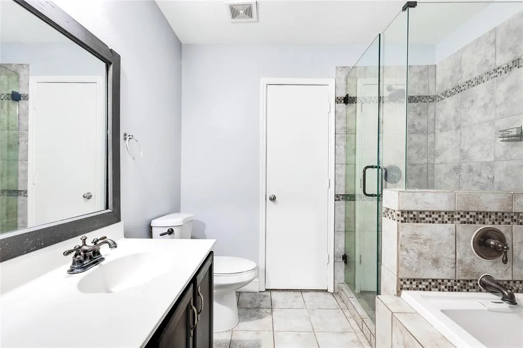 Vanity with integrated sink, dark wood-finish cabinetry, framed mirror, glass-enclosed shower, and tiled tub surround