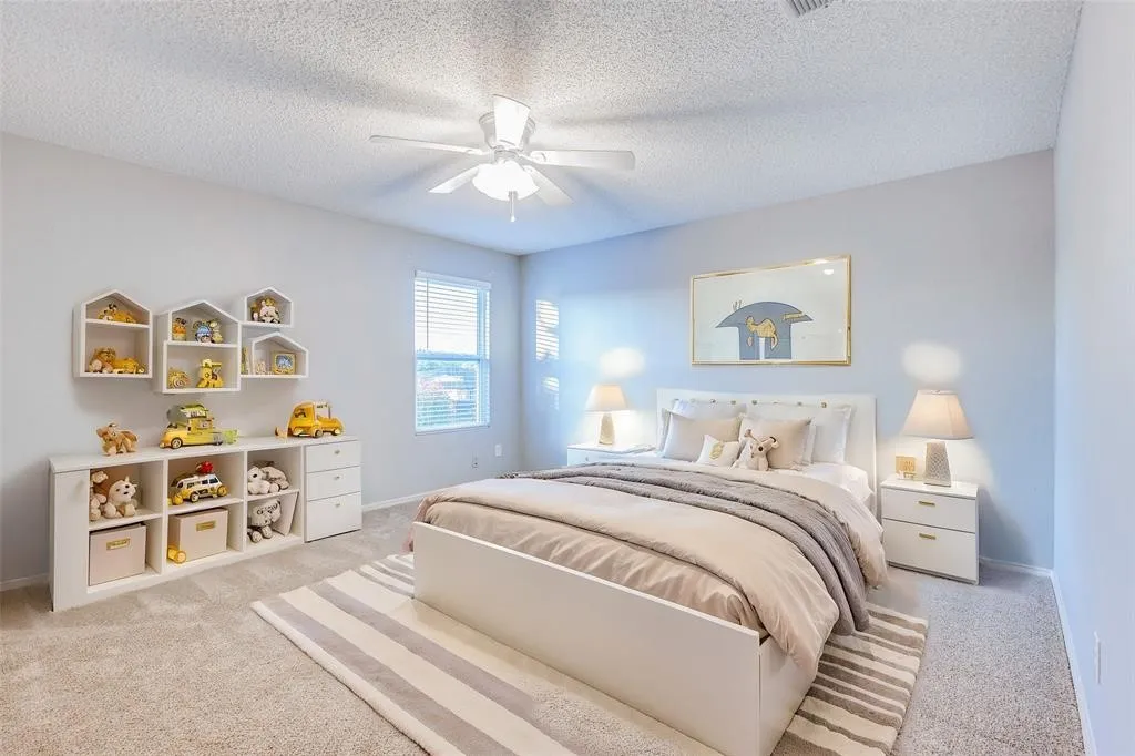Recessed window with horizontal blinds, overhead ceiling fan, soft gray wall paint, and light-toned carpet flooring