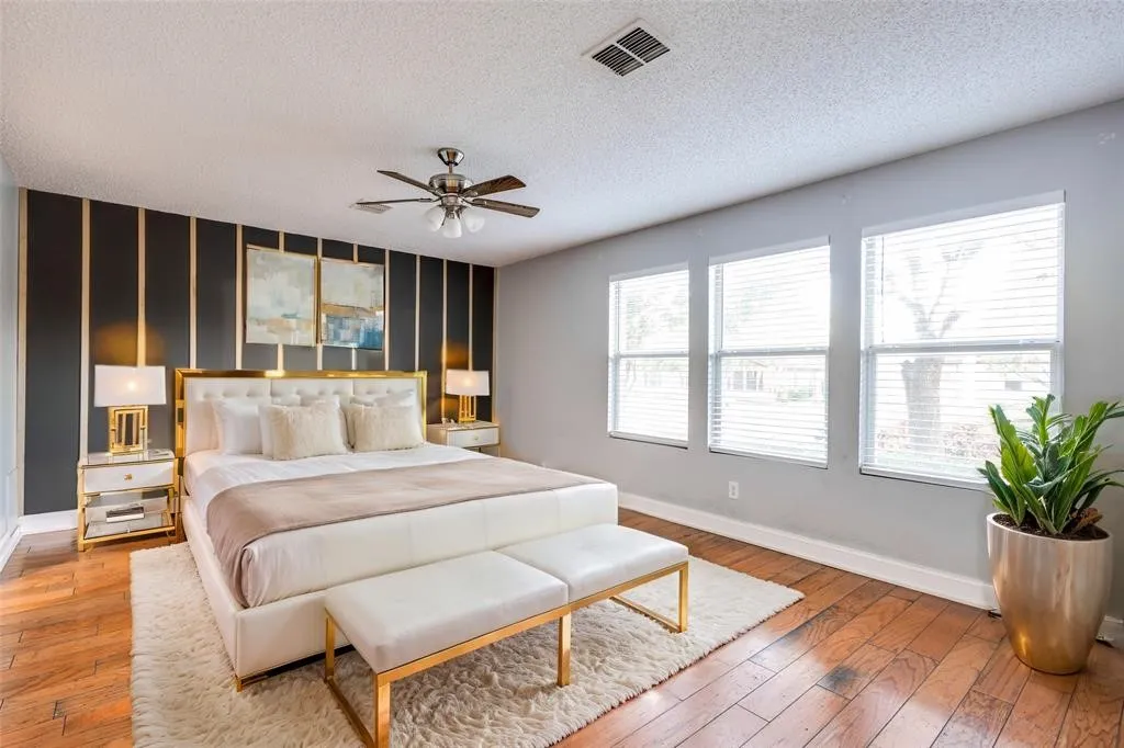 Wood-finish flooring, multiple windows with blinds, ceiling fan, and decorative wall paneling