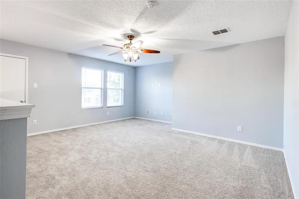 Expansive carpeted room featuring a ceiling fan, multiple windows, and light gray wall finishes
