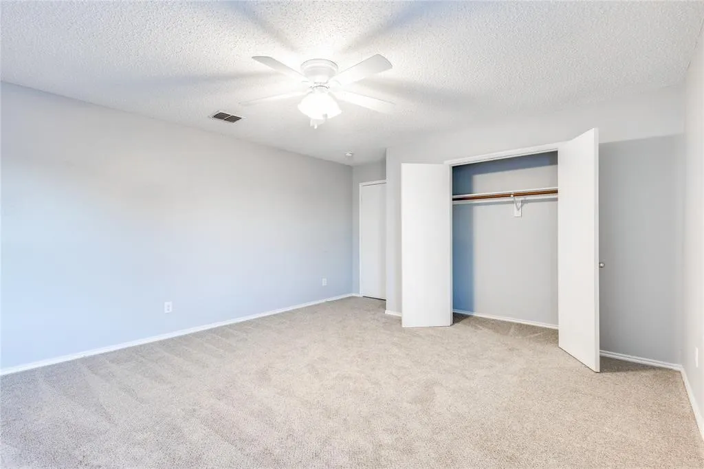 Neutral tone wall paint, textured ceiling, ceiling fan with integrated lighting, built-in closet with bi-fold doors, and neutral carpet flooring