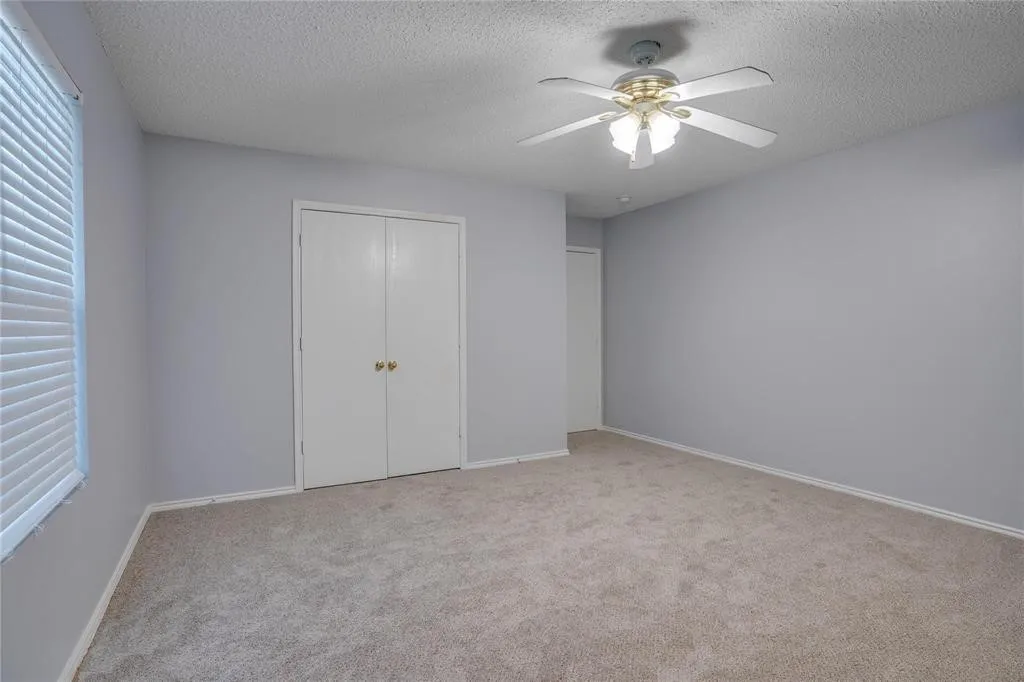 Carpeted room featuring a ceiling fan with integrated lighting, window blinds, and bi-fold closet doors