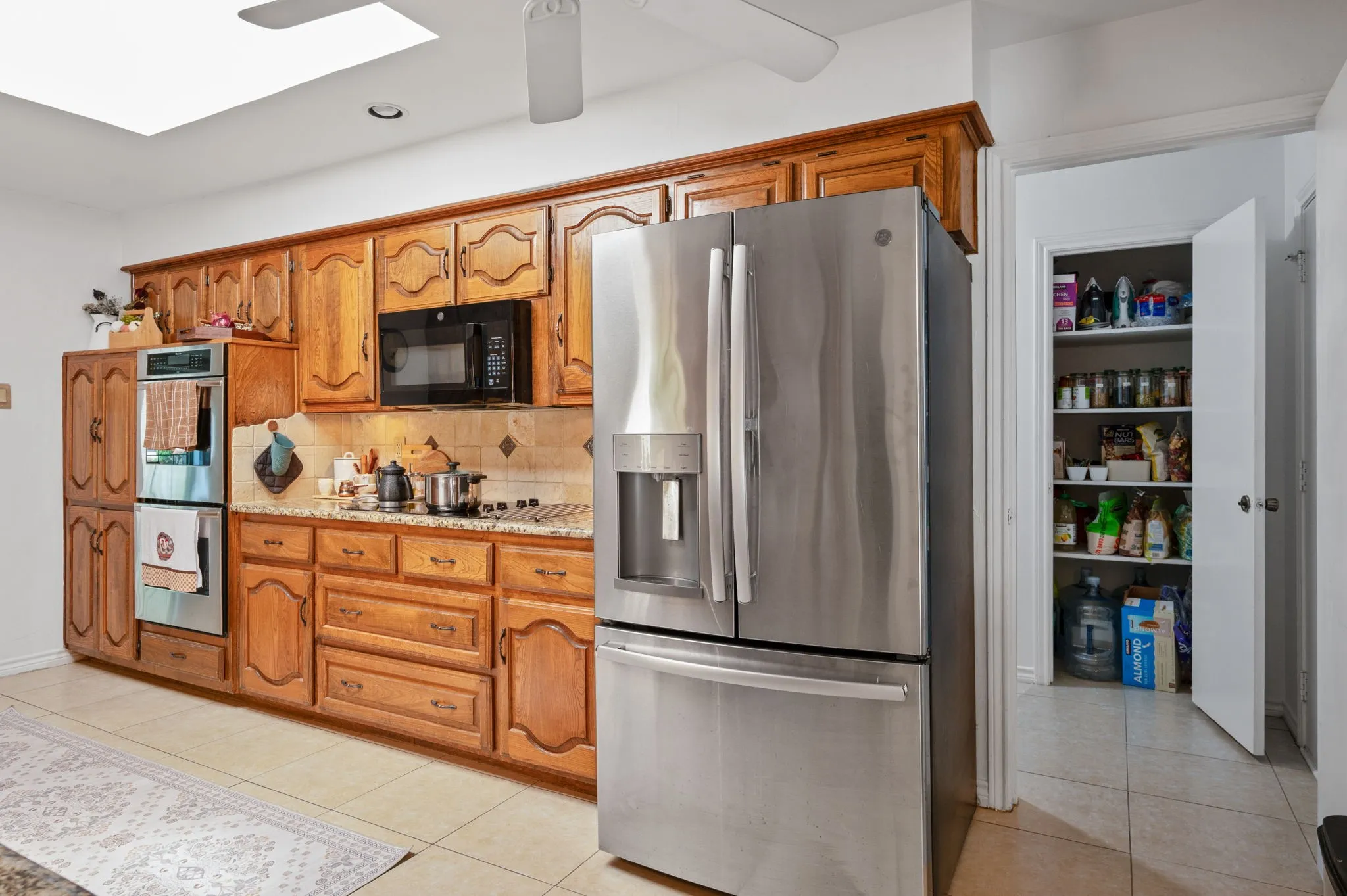 Kitchen featuring wood cabinetry, stainless steel appliances, a tiled backsplash, and a skylight