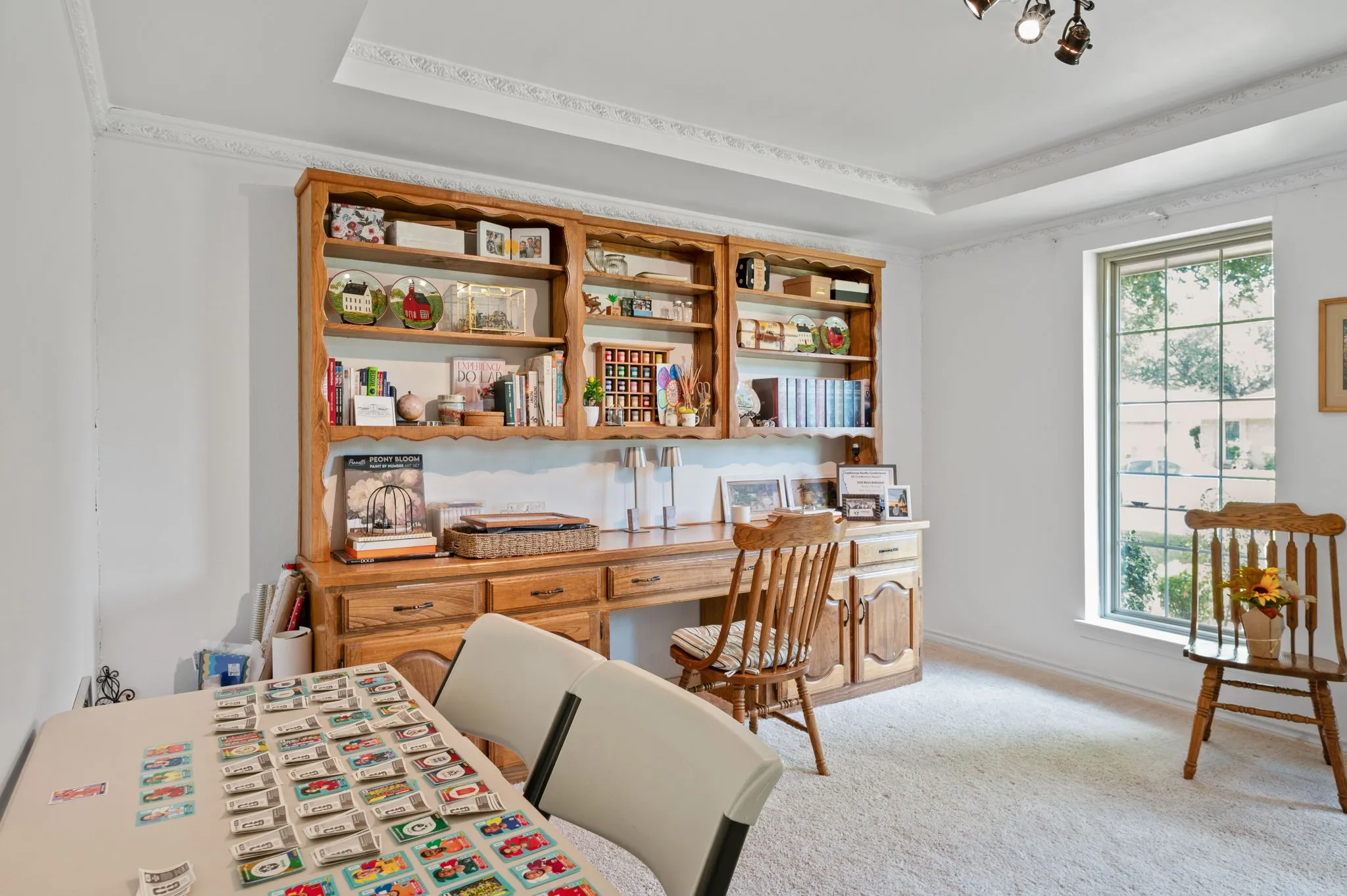 Built-in wood-finish shelving and desk unit, tray ceiling with decorative molding, recessed window, and wall-to-wall carpeting