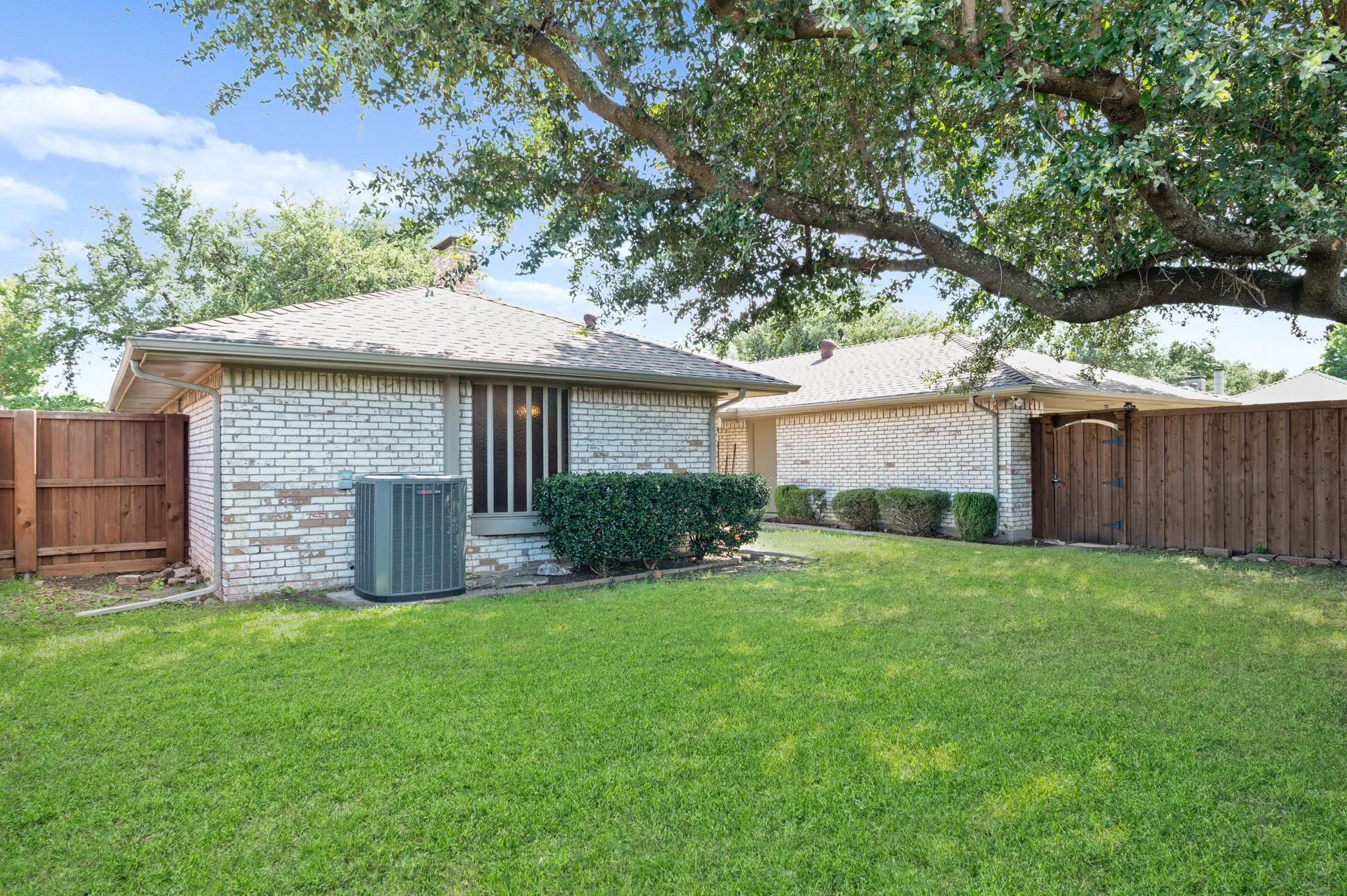 Expansive green lawn with mature tree, brick exterior, and wood fencing