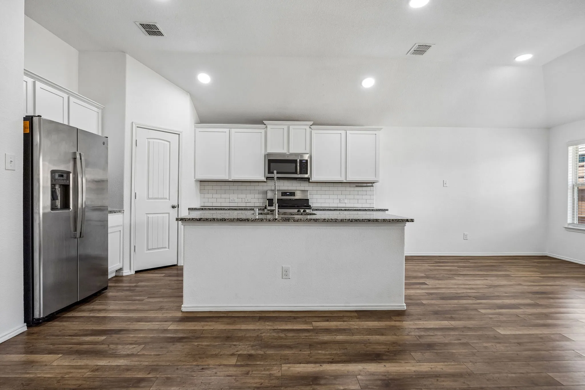 Kitchen featuring a central island, white cabinetry, stainless steel appliances, and wood-finish flooring