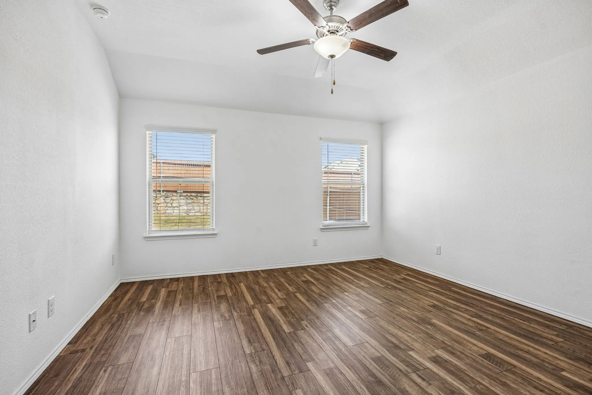 Bright room with wood-finish flooring, two windows with blinds, and a ceiling fan with integrated lighting