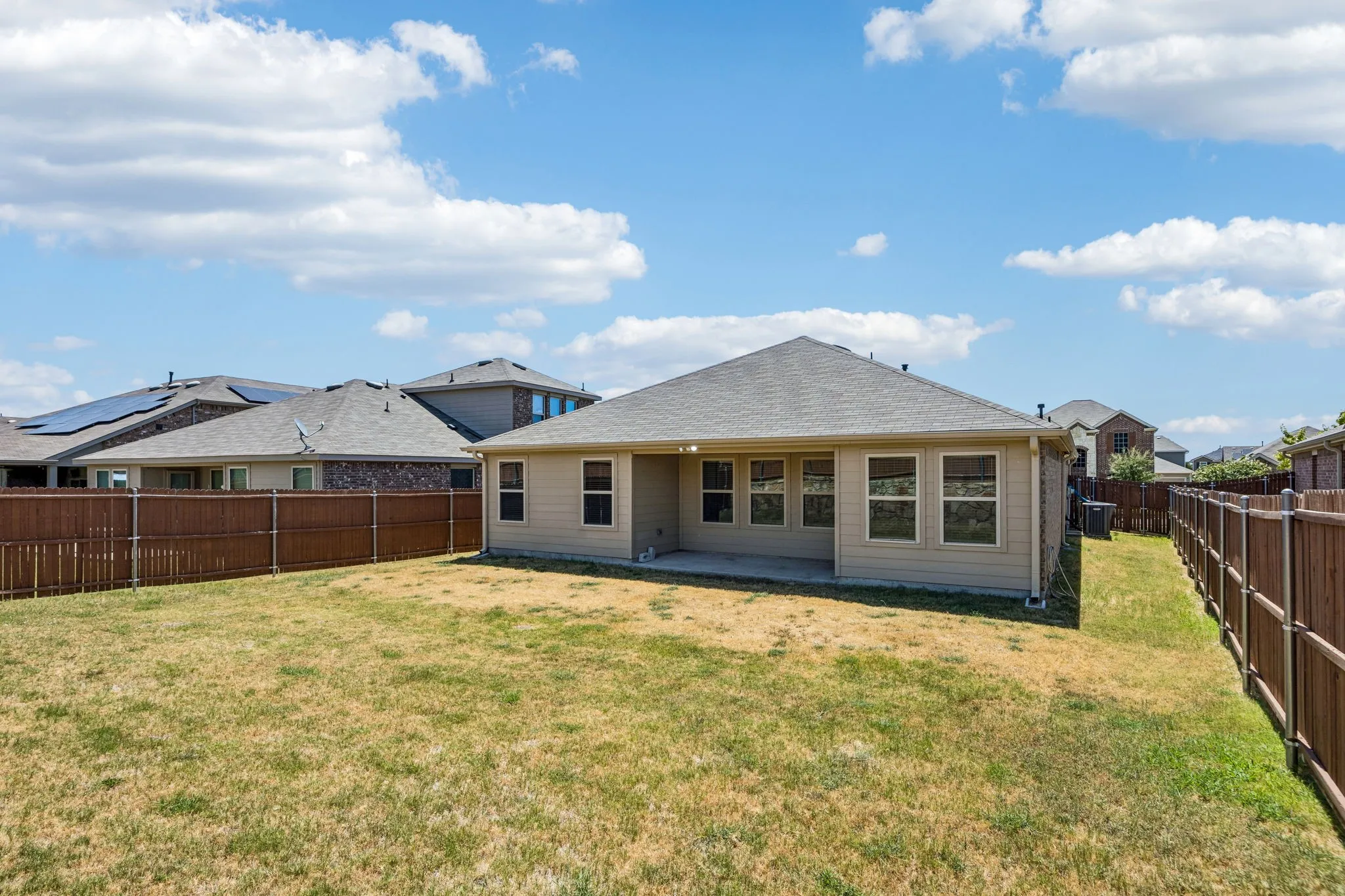 Expansive backyard featuring a privacy fence, concrete patio, and multiple windows along the rear exterior