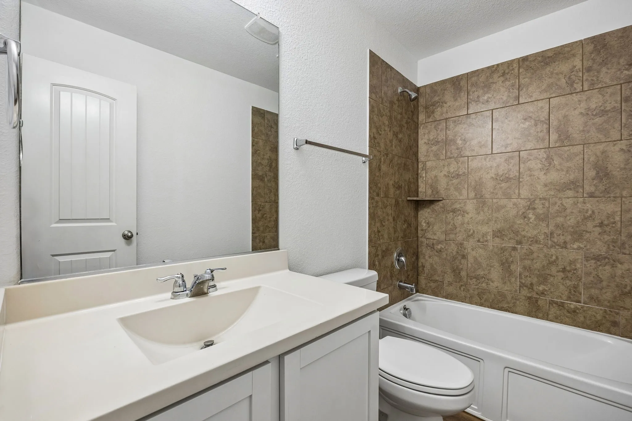 White vanity with integrated sink, chrome faucet, full-width mirror, and a tiled shower/tub combination